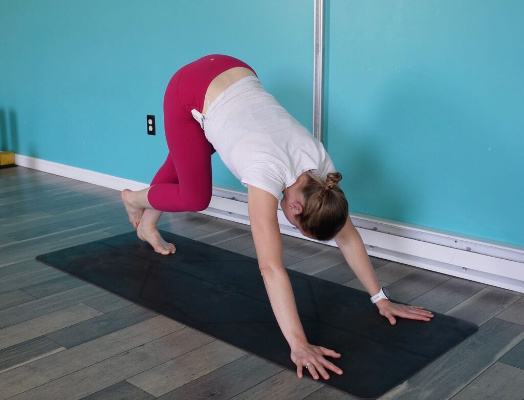 Dr. Chloe pushing through both hands with her hips extended behind her. Her weight is pushed back into her left leg with her right foot tucked behind her left ankle as a yoga pose for runners